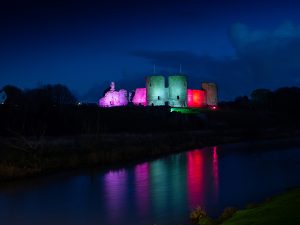 Rhuddlan Castle lit up in multi colour lighting at night.